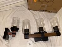 Close-up view of the single-light wall sconce and 3-light vanity fixture highlighting the faux wood grain accents, cylindrical glass shades, and black/dark bronze finish.