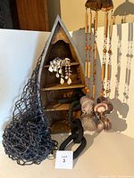 Overall lot showing all items including the wooden boat shelf, shell curtain tiebacks hanging on it, hanging shell and wood wind chime, large black faux chain, and knotted nautical fishnet.