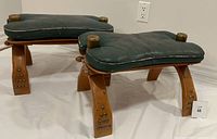 Pair of mid-century footstools upholstered in green vinyl with brass corner caps and studded curved wood legs, showing wear and patina.