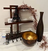 Full view of the collection arranged together showing all items, including the staggered wooden shelf, black Eiffel Tower wire sculpture, cast iron 'PARIS' wall hook, tall striped vase, metallic gold-lined bowl, and pink berry garland.