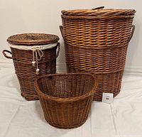 Set of 3 woven wicker baskets including tall lidded hamper, medium lidded basket with liner, and wide open basket, shown grouped on white surface.
