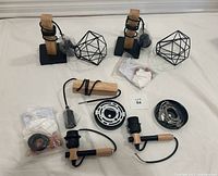 Four disassembled wall sconces laid out on a flat surface showing black metal mounting plates, natural wood grips, black sockets, cords, and matte black geometric cage shades.