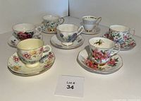 Seven assorted vintage English bone china teacup and saucer sets arranged on a white surface showing various floral designs and gold trim.