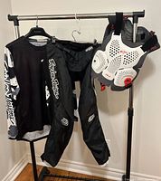Full view of the Troy Lee Designs motocross pants, jersey, and Alpinestars chest protector hanging on a metal rack.