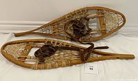Pair of vintage wooden snowshoes with rawhide webbing and leather bindings laid side by side on white background