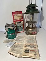 Photo showing green Coleman lantern, green Coleman Model 505A Easi-Lite stove, original box, and instruction manuals laid out on white background.