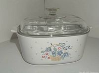 Front view of CorningWare casserole dish showing the Spring Blossom floral basket design and clear glass lid on top.