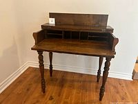 Front view of the vintage wooden letter desk showing the open hinged top with six small cubbies inside, and turned spindle legs.