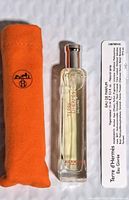 Photo showing the Hermès perfume spray bottle along with its bright orange fabric pouch and an information card.
