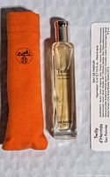 Photo showing the Hermes perfume spray bottle, orange fabric pouch, and informational insert.