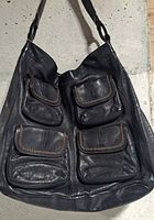 Front view of the grey leather bag showing four flap pockets with decorative stitching.