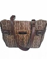 Front view of brown canvas handbag with repeating Etienne Agner logo pattern, leather trim, front leather brand patch, and shoulder straps.