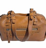 Front view of tan leather handbag with front zipper pocket and double buckle strap detail.