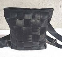 Front view of the Harveys grey woven seatbelt backpack showing woven square pattern and top zipper area, along with shoulder straps lying flat