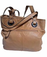 Front view of tan leather handbag with zippered exterior pocket and two short handles.