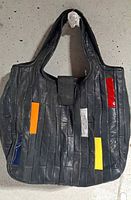 Front view of the handbag showing gray leather with rectangular multicolored leather accents in orange, red, yellow, blue, and silver-gray patches, two shoulder straps, and flap closure.