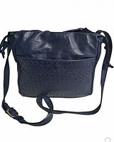 Front view showing woven textured leather pocket, adjustable sling strap with buckle and side tassels.