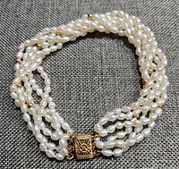 Six-strand freshwater pearl bracelet arranged in a circle on grey fabric showing overall design and clasp.