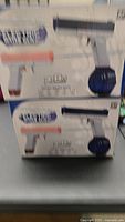Blurry image of two boxed electric water guns showing the product image and packaging.