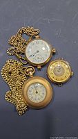 All three pocket watches laid out with two on chains and one small watch