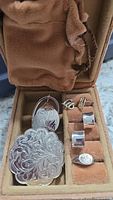 Travel jewelry box open with multiple pairs of engraved and plain sterling silver earrings arranged inside along with a small brooch