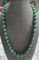 Front view of the full 18-inch necklace showing uniform green aventurine round beads on display stand.