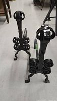 Pair of black cast iron fireplace andirons showing the top and front decorative scroll design and fleur-de-lis finial.