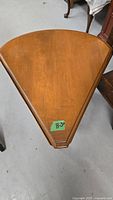 Photo showing the triangular folded corner table with wood finish and a green label on top.