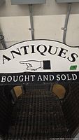 Front view of black and white vintage metal antiques sign with 'ANTIQUES BOUGHT AND SOLD' text and pointing hand graphic.