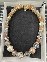 Front view of the 18-inch amber-colored crystal necklace featuring faceted beads, faux pearls, and rhinestone spacer beads laid flat on a black velveteen pouch.