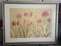 Framed print of red amaryllis flowers with green leaves on beige background, decorative silver frame.