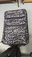 Leopard print suitcase with several zippered outer compartments, fabric design, and visible wear on exterior