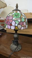 Lamp unlit showing Tiffany style floral stained glass shade in pastel colors and antique brass metal base.