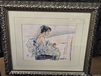 Framed artwork of the resting ballerina showing entire piece in ornate silver frame with decorative floral border and matting around the print.