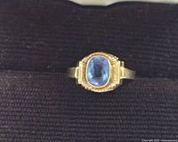 Top-down view of gold ring with oval blue topaz set in bezel and decorative shoulders