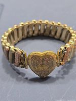 Close-up of heart-shaped centerpiece of the tri-color metal sweetheart bracelet showing engraving and stretch band segments.