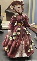 Front view of the vintage ceramic figurine showing the Victorian lady in a burgundy dress with white flower accents and gold trim.