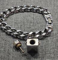 Silver-tone chunky interlocking chain bracelet laid flat with small rectangular perfume bottle charm detached showing inside of the charm and removable screw-top with ball-tipped applicator.