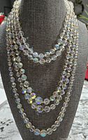 Three vintage necklaces displayed on a gray fabric bust including two crystal bead necklaces of different lengths.