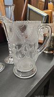 Close-up of vintage clear glass pitcher with embossed decorative pattern and beaded rim