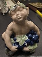 Front view of the porcelain faun figurine holding grapes showing facial features and grape cluster.