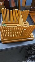 Wooden bamboo bread slicer on black table, showing the folding vertical guides and sliding mechanism.