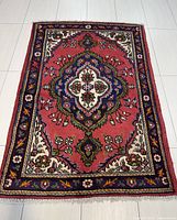 Top-down view of full Persian Tabriz rug on white tiled floor showing overall design and condition.