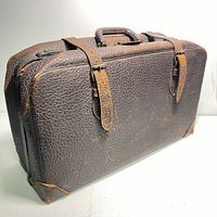 Front angled view of the brown leather vintage suitcase showing texture, straps, handle and some wear