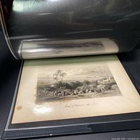 Photo of a pastoral landscape etching showing sheep grazing near palm trees and hills in the distance, inside a protective portfolio sleeve.