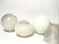 Four antique glass lamp shades grouped together on a white surface showing different shapes and visible wear.
