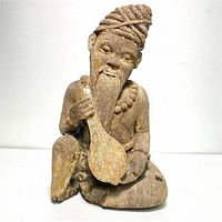 Front view of antique carved wood figure showing bearded man with turban playing sitar, revealing paint remnants and detailed facial features.