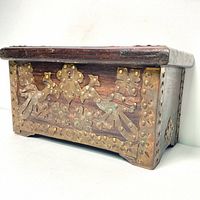 Side front angle showing detailed bronze decorations on the wood chest including floral and geometric bronze motifs attached with rivets on the front panel.