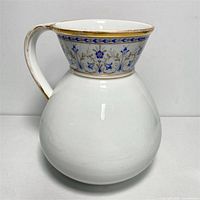 Front view of the antique porcelain water jug showing the white bulbous body and decorative neck with blue floral patterns.