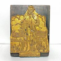 Front view of brass printing block showing the detailed figure and background design mounted on the wooden base.